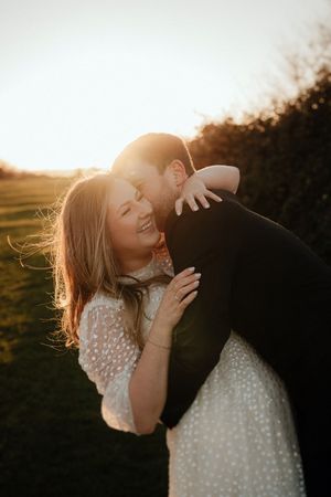 A couple embraces in a romantic sunset moment, with warm golden light creating a dreamy silhouette effect.