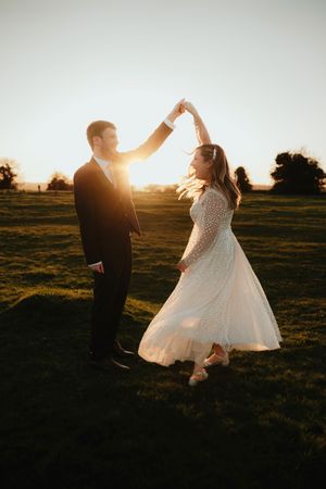 A couple dances together in a golden sunset field, with the bride's white dress twirling gracefully in the light.