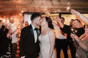 Bride and groom share a kiss surrounded by wedding guests holding sparklers during a romantic indoor reception sendoff.