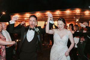 Joyful newlyweds exit wedding reception through sparkler send-off, bride in beaded gown and groom in black tuxedo.