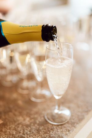 Aqualia champagne being poured into a flute glass with a row of empty glasses in the background.