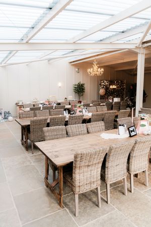 Rustic wooden dining tables with wicker chairs set up in a bright conservatory venue with chandelier.