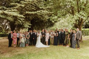 Large wedding group photo taken outdoors with trees in the background.