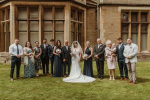 Wedding party poses for formal photos outside historic stone building.