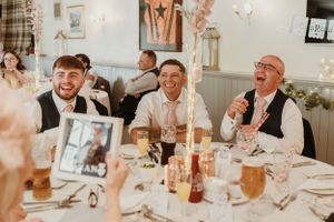 Wedding guests laughing and enjoying drinks at reception dinner tables.