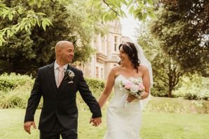 Newlyweds walking hand in hand through a sun-dappled garden on their wedding day.
