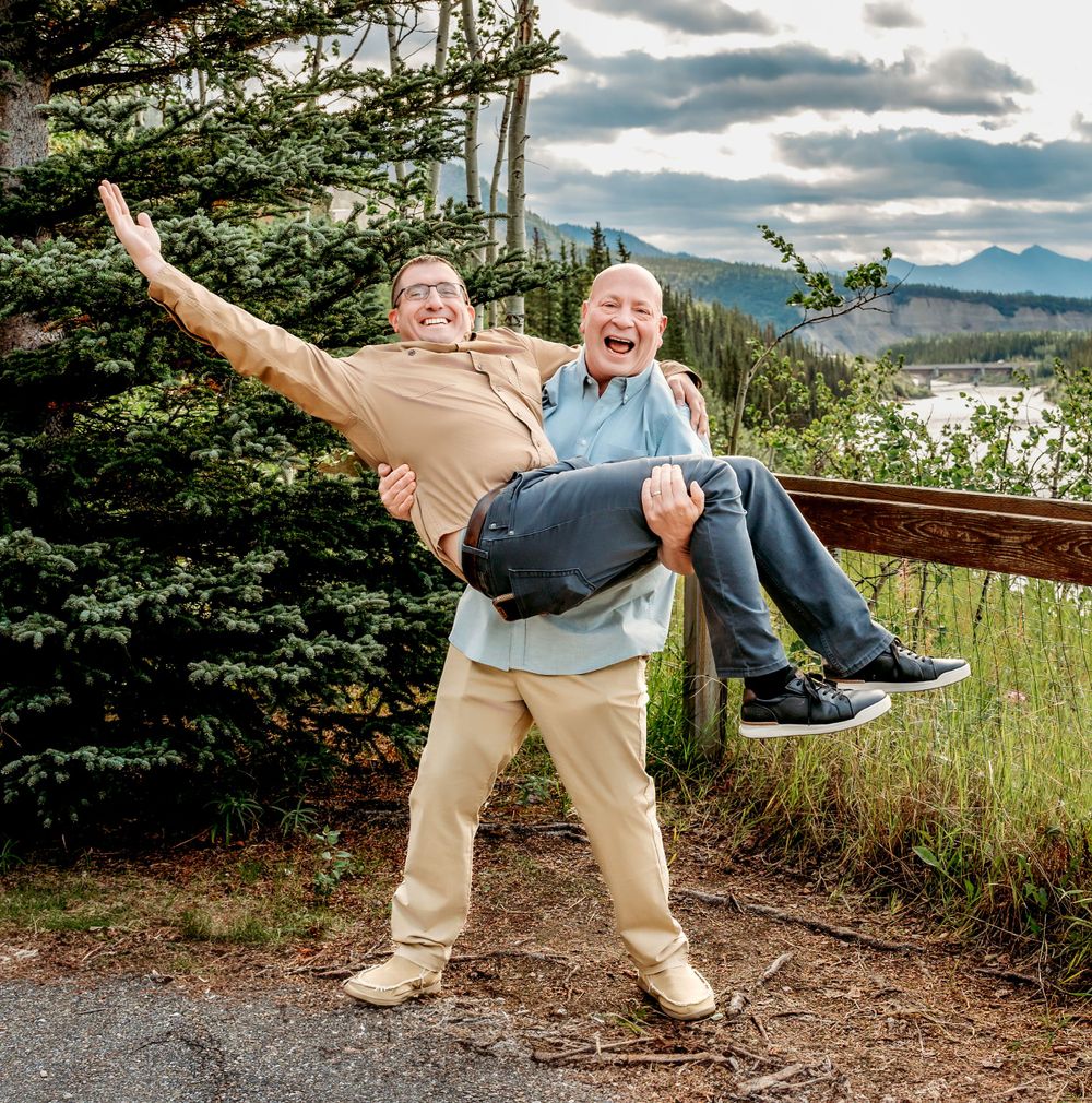 Playful moment on mountain path as one person lifts another against scenic mountain backdrop.