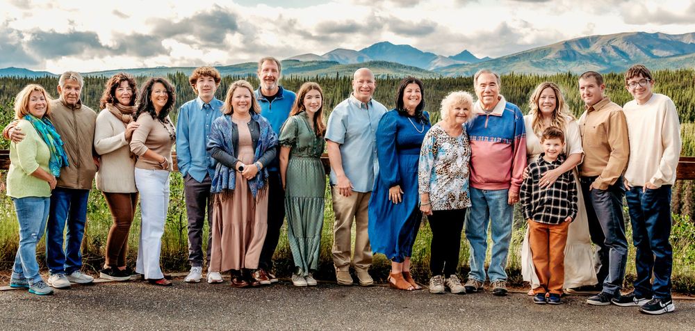 Large group photo of people dressed in casual attire with mountain vista background.