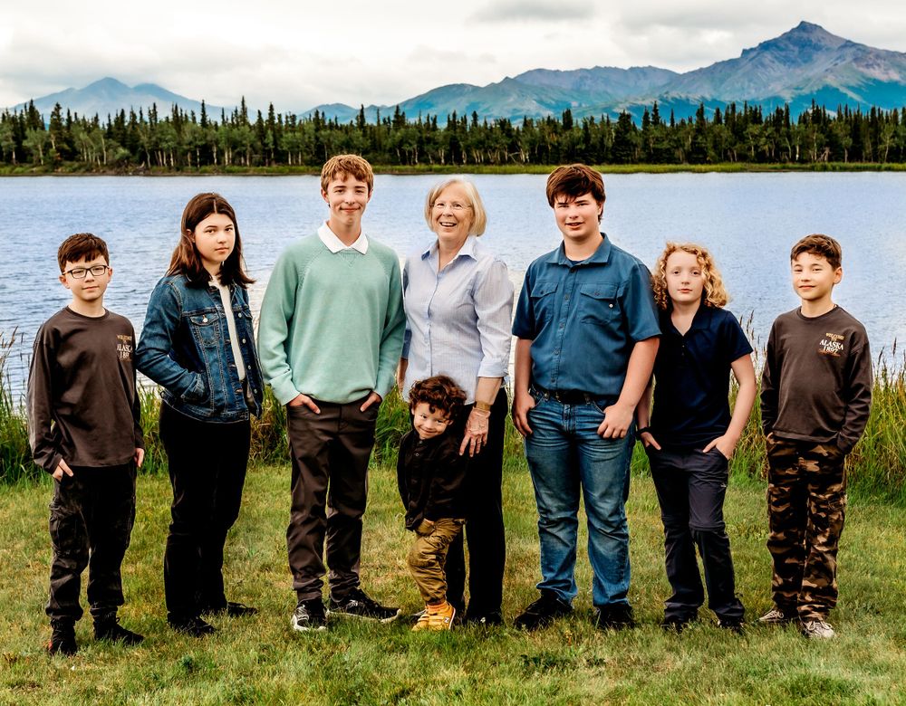 Family group posing beside a lake with mountain backdrop in Alaska.