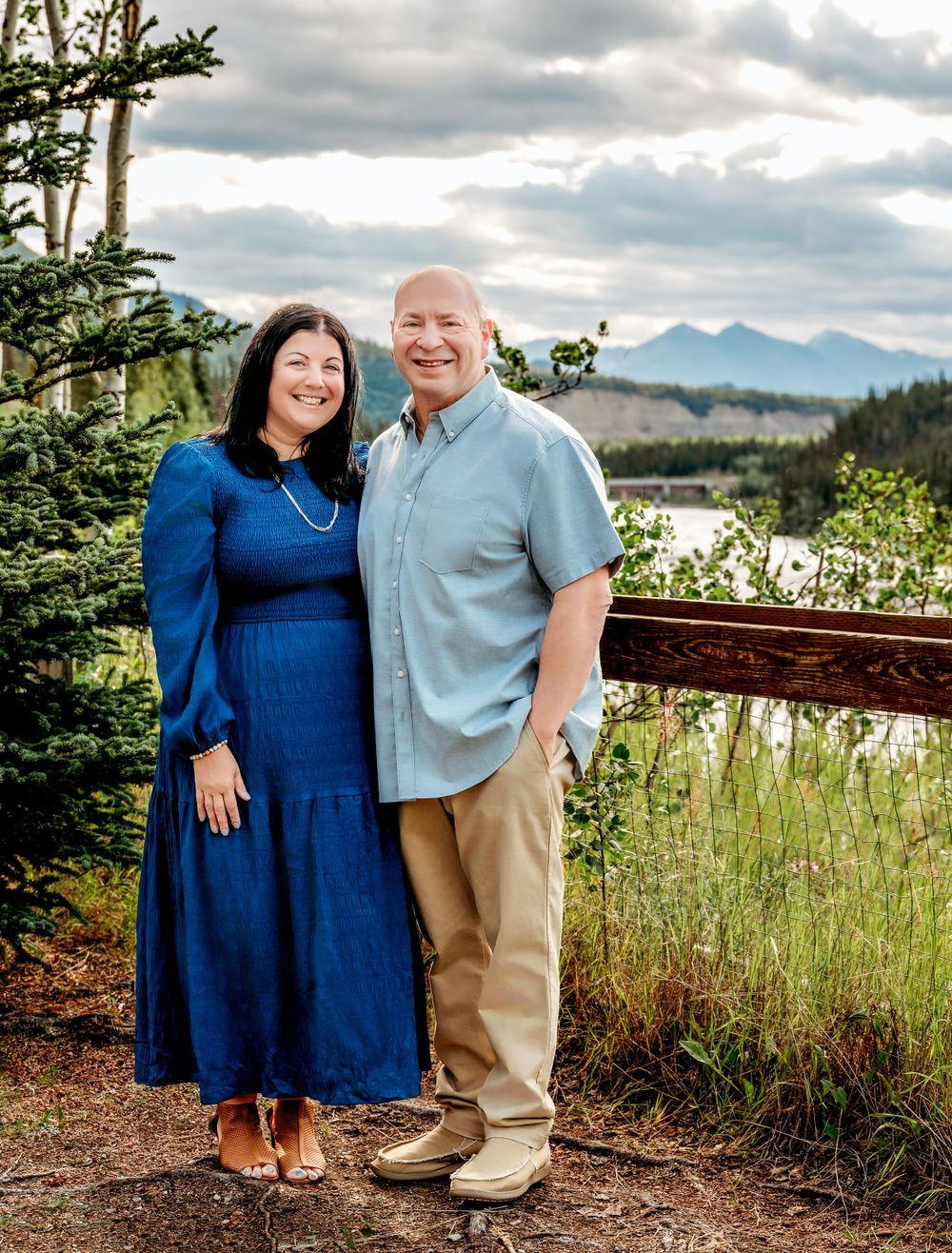 Couple in blue and khaki standing in front of mountain landscape.