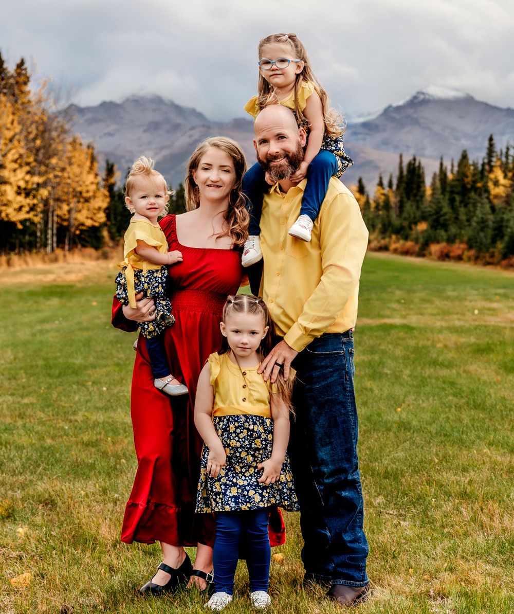 Family portrait with mountain backdrop wearing coordinated red, yellow and floral outfits.