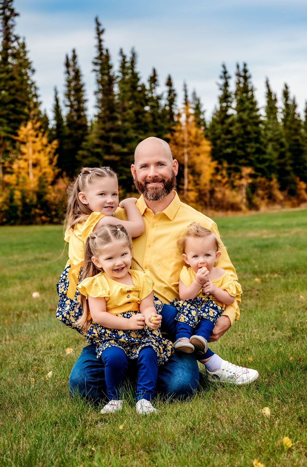 Joyful group portrait with yellow and floral outfits against mountain scenery.