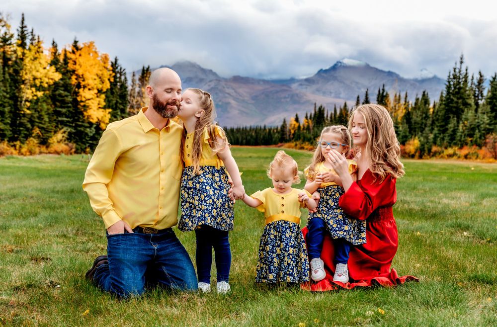 Family group in coordinating yellow and red outfits enjoying autumn mountain scenery.