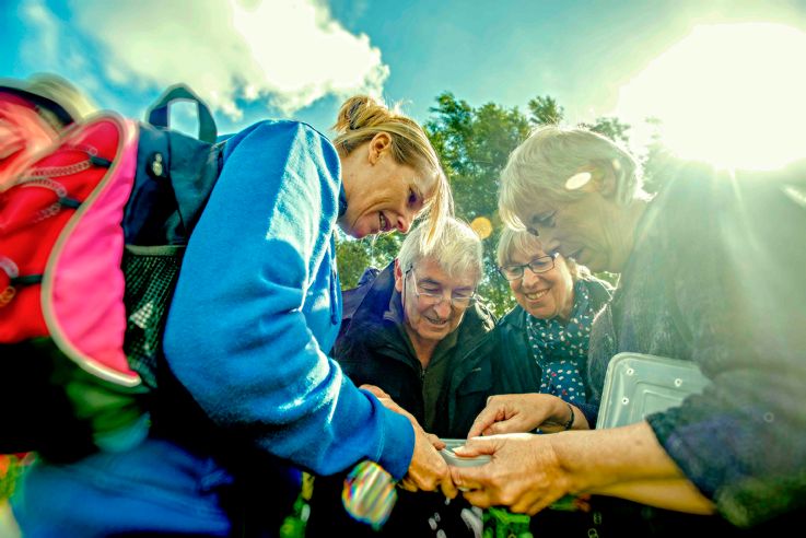 A Suffolk Wildlife group of elderly people gathered outdoors on a sunny day, looking at inserts found in the health.