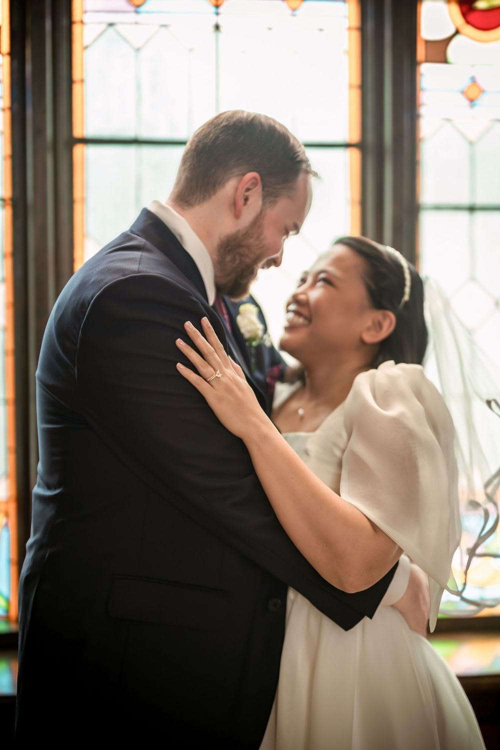 Bride and groom share a tender moment in front of a stained glass window during their wedding ceremony.
