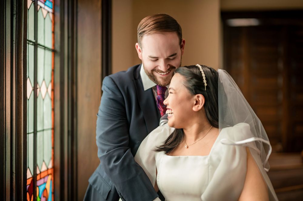 Joyful bride and groom sharing a tender moment near stained glass windows on their wedding day.