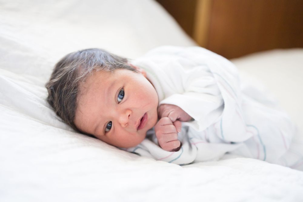 Newborn baby with dark hair lying on white bedding, during her Fresh 48 session at Fort Sanders Medical Center in Knoxville.