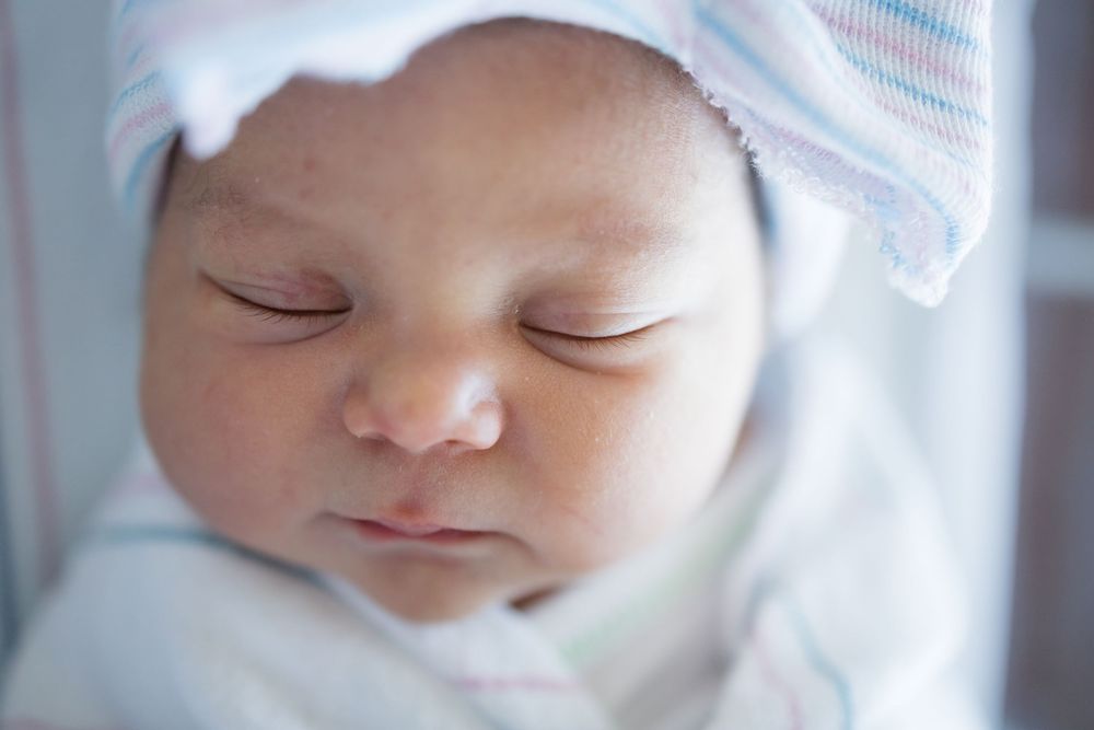 Peaceful newborn baby sleeping in a striped hospital hat during her Fresh 48 session at Fort Sanders in Knoxville, TN.