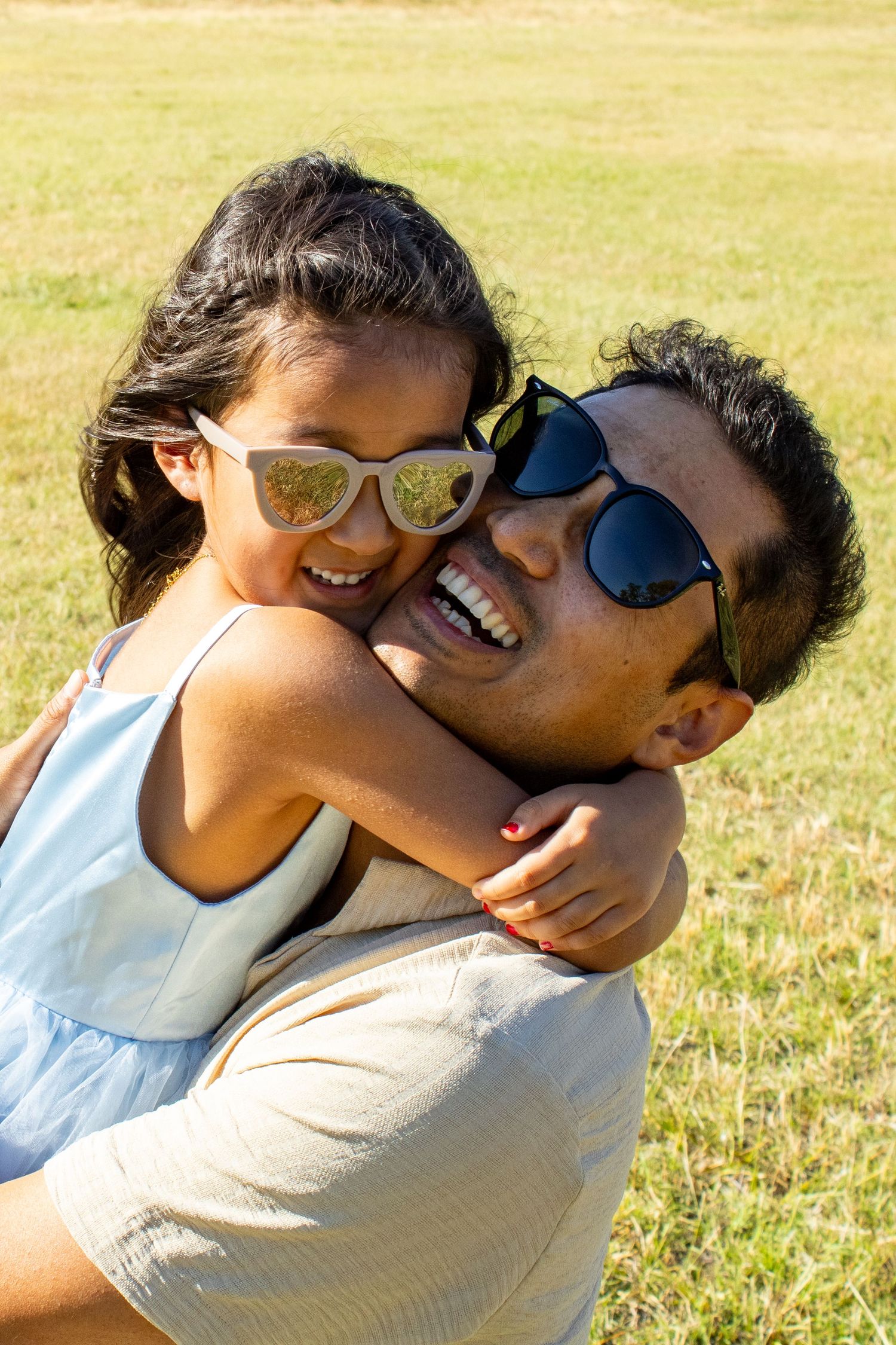 A laughing father and daughter wearing sunglasses share a joyful piggyback moment outdoors.