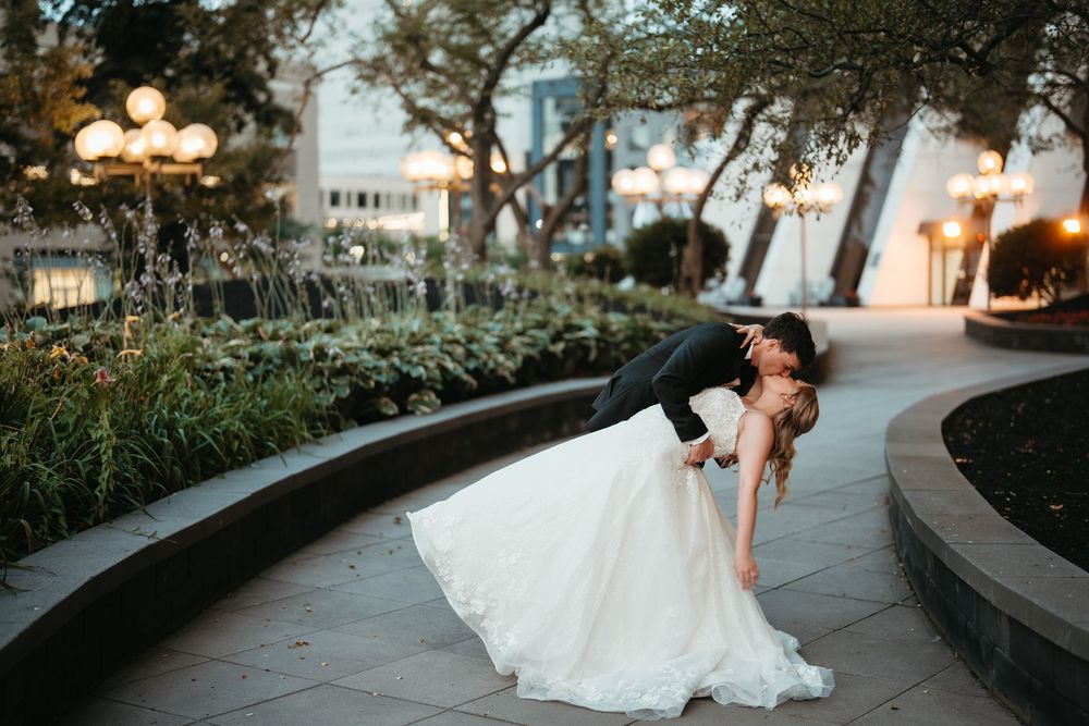 Bride and groom share a romantic dip kiss in an elegant outdoor garden setting at dusk during their wedding.