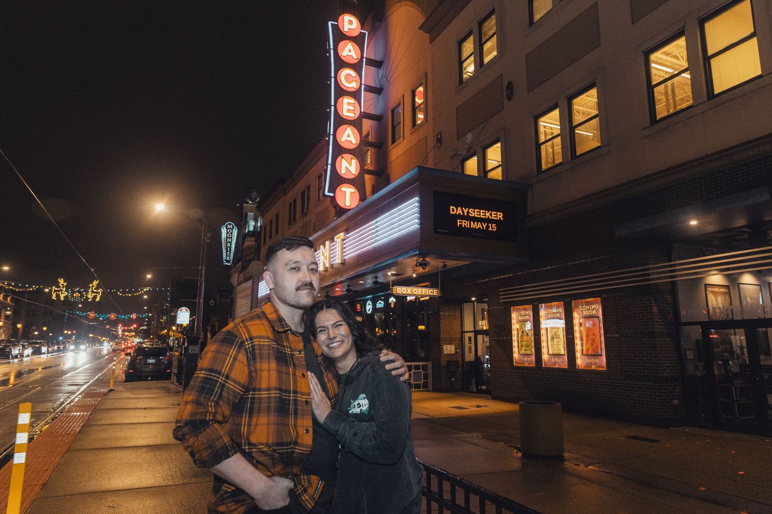 Couple embracing at night outside a lit theater marquee on a city street.