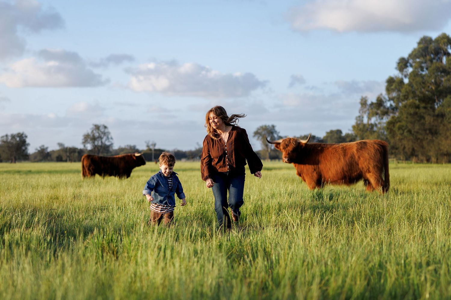 Mum and child running through a field with highland cows