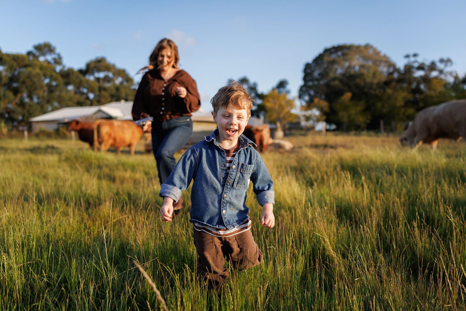 Mum and child running through a field with highland cows
