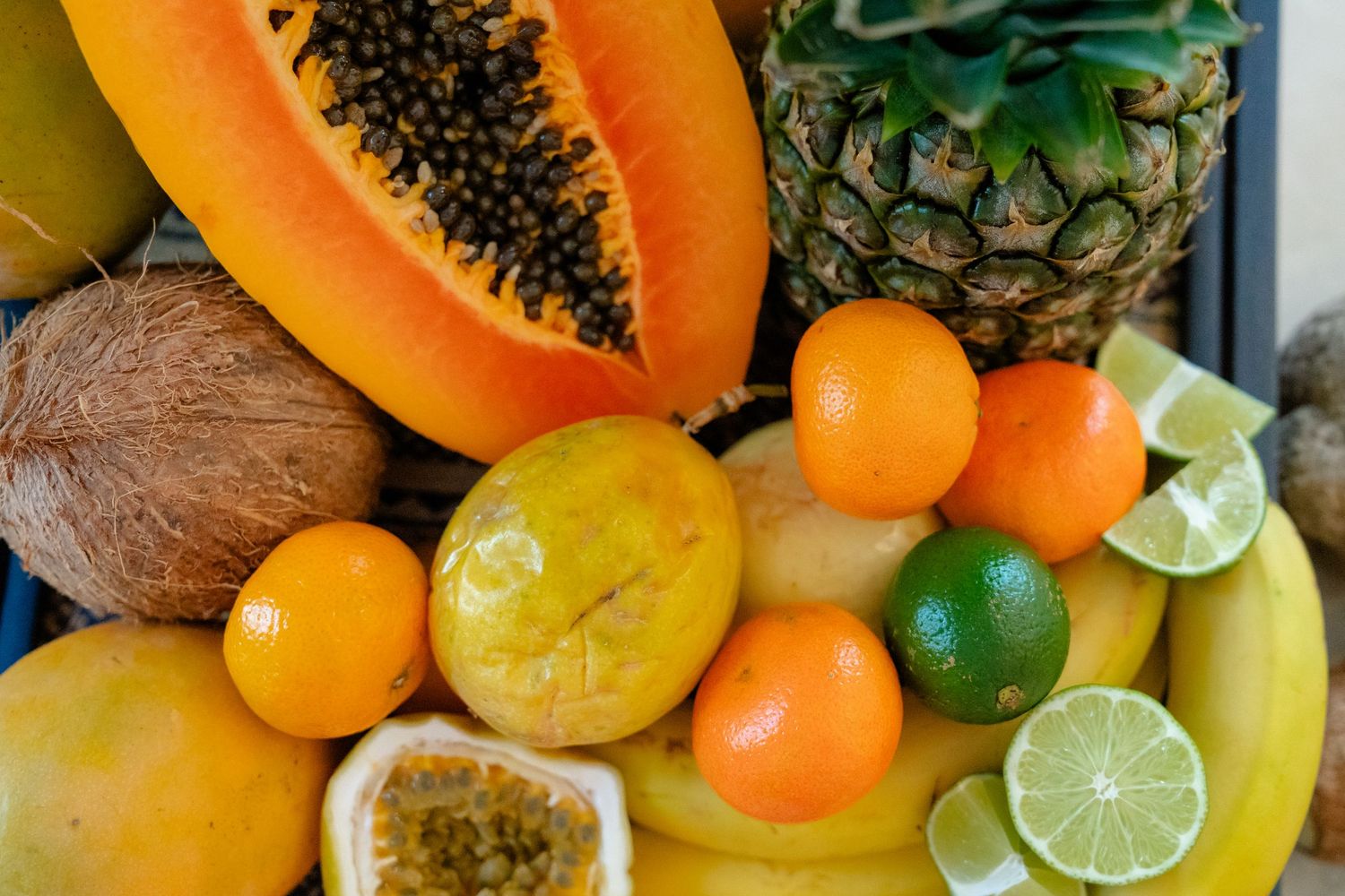Colorful tropical fruits including papaya, pineapple, coconut, mandarins, lime, banana, and passion fruit arranged together.