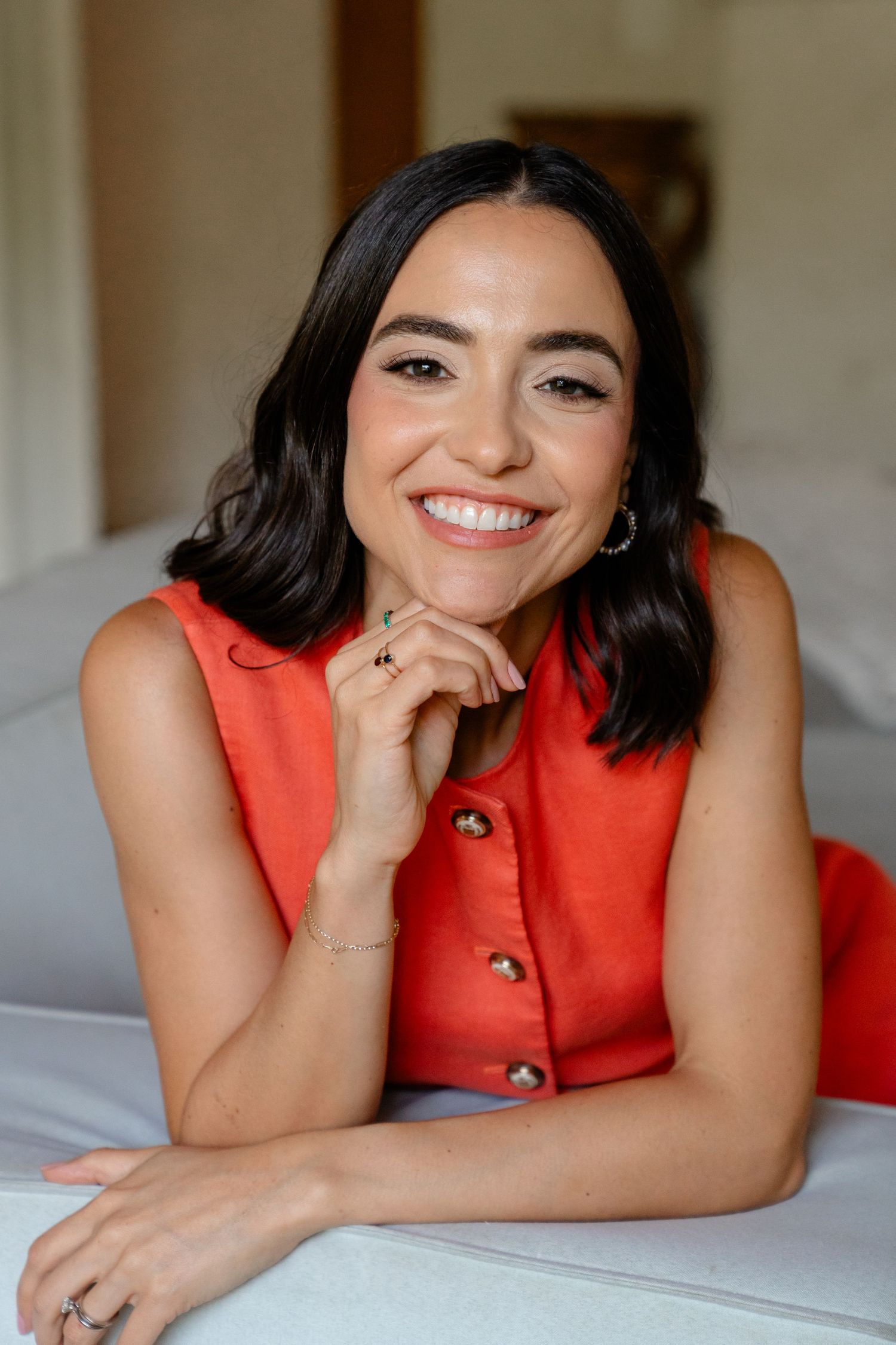 Smiling young woman with dark hair wearing a red sleeveless dress, posing with chin resting on hand.