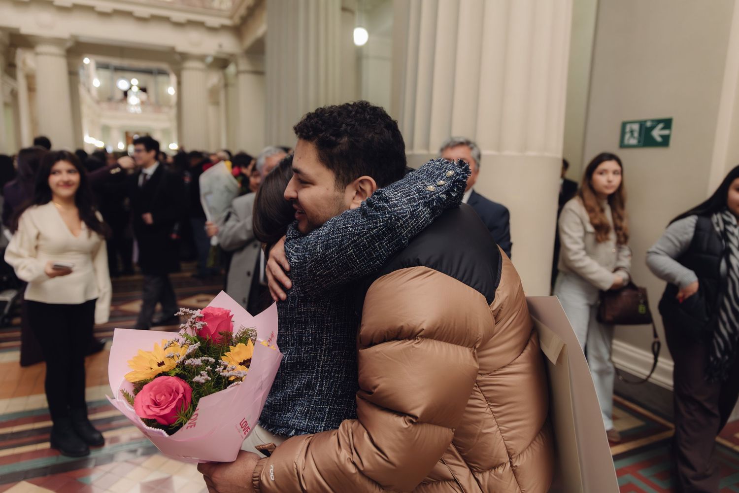 Two people sharing a warm embrace with colorful flower bouquet at a graduation celebration event.