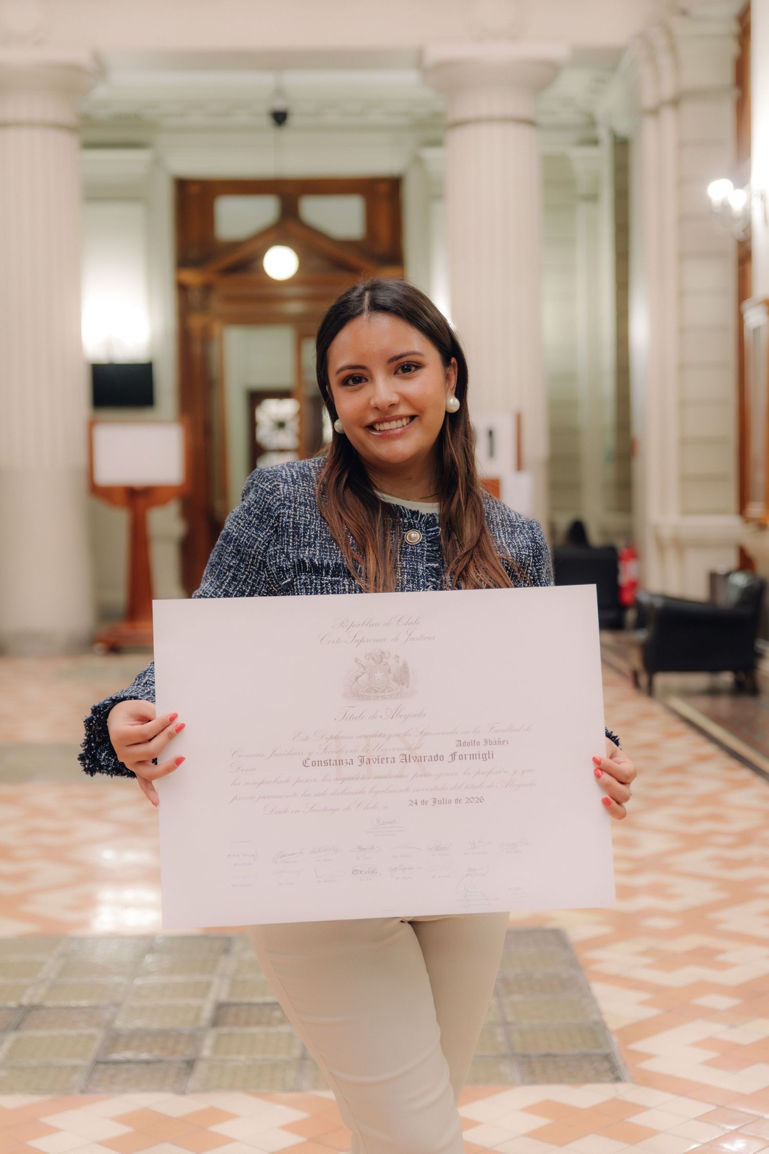 Happy young woman in blue tweed jacket holding official graduation diploma certificate while smiling.