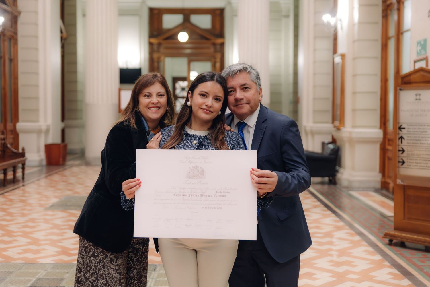 Young graduate displays diploma with family in ornate building.