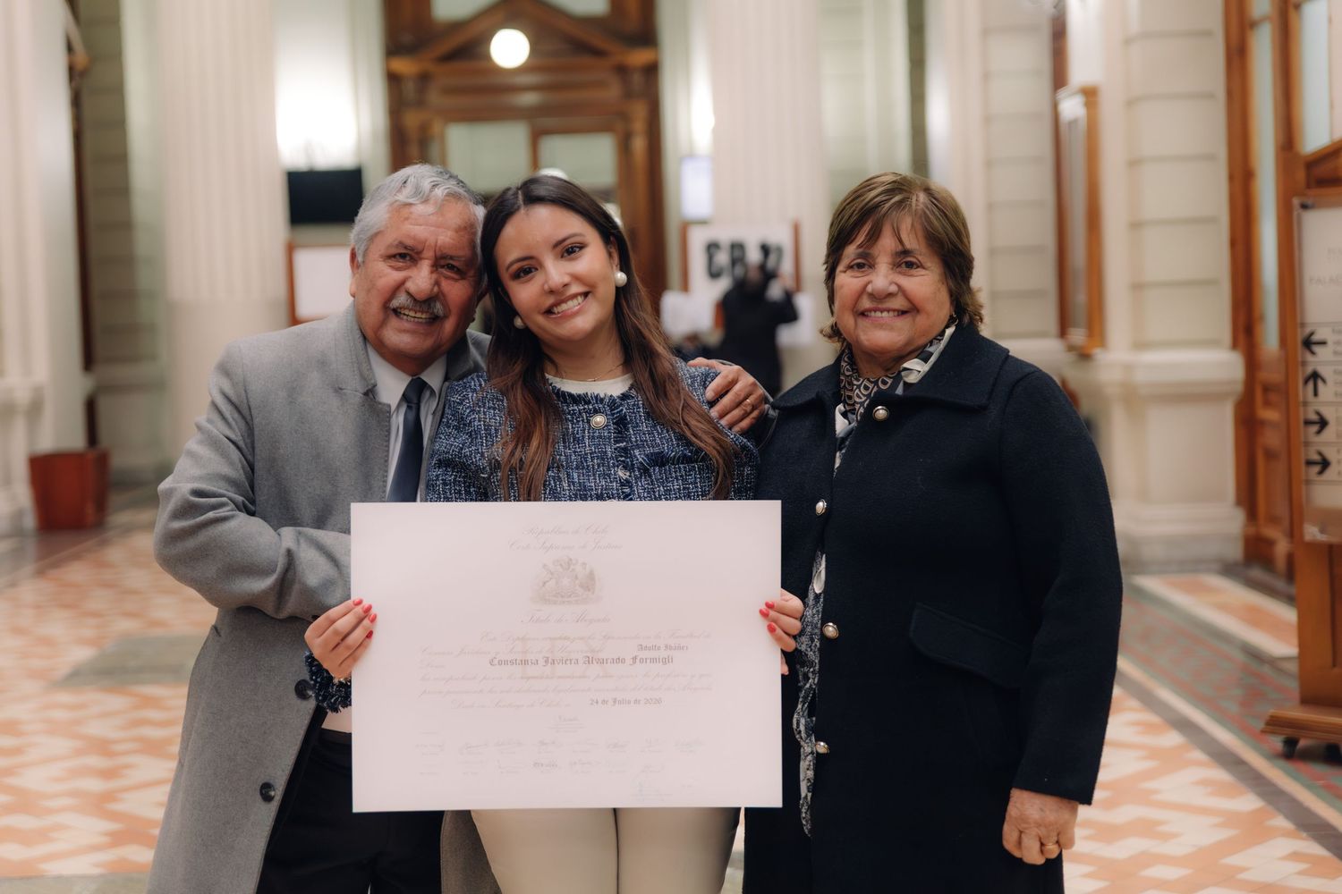 Graduate holds certificate with elderly couple in formal hall.