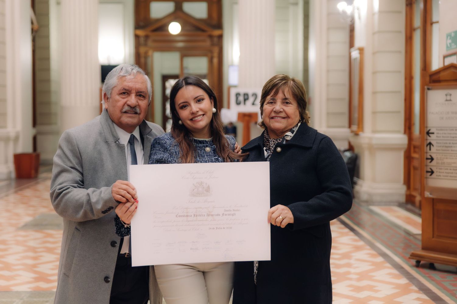 Young woman displays official diploma with grandparents indoors.