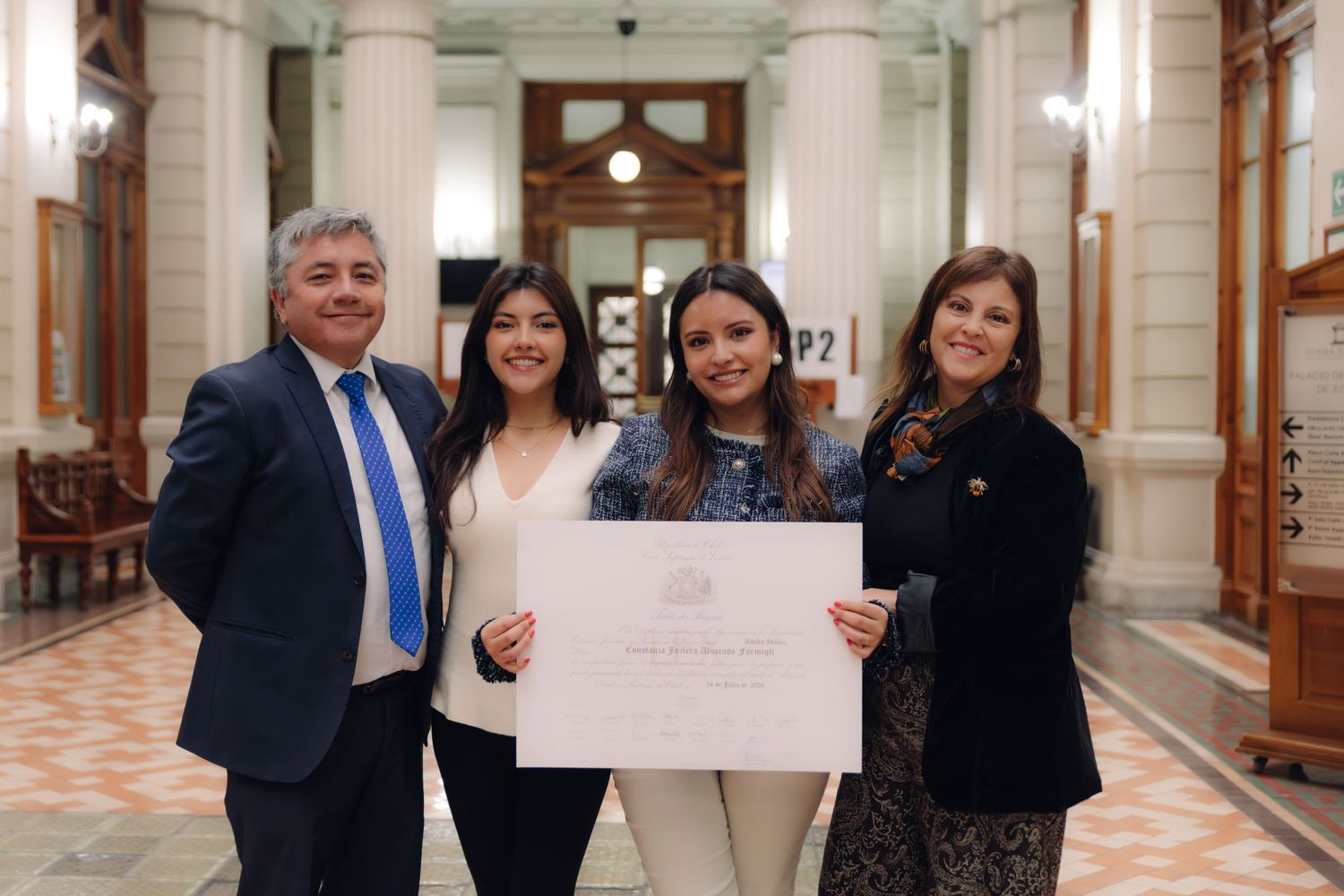 Four people smile holding a certificate in a grand institutional corridor.