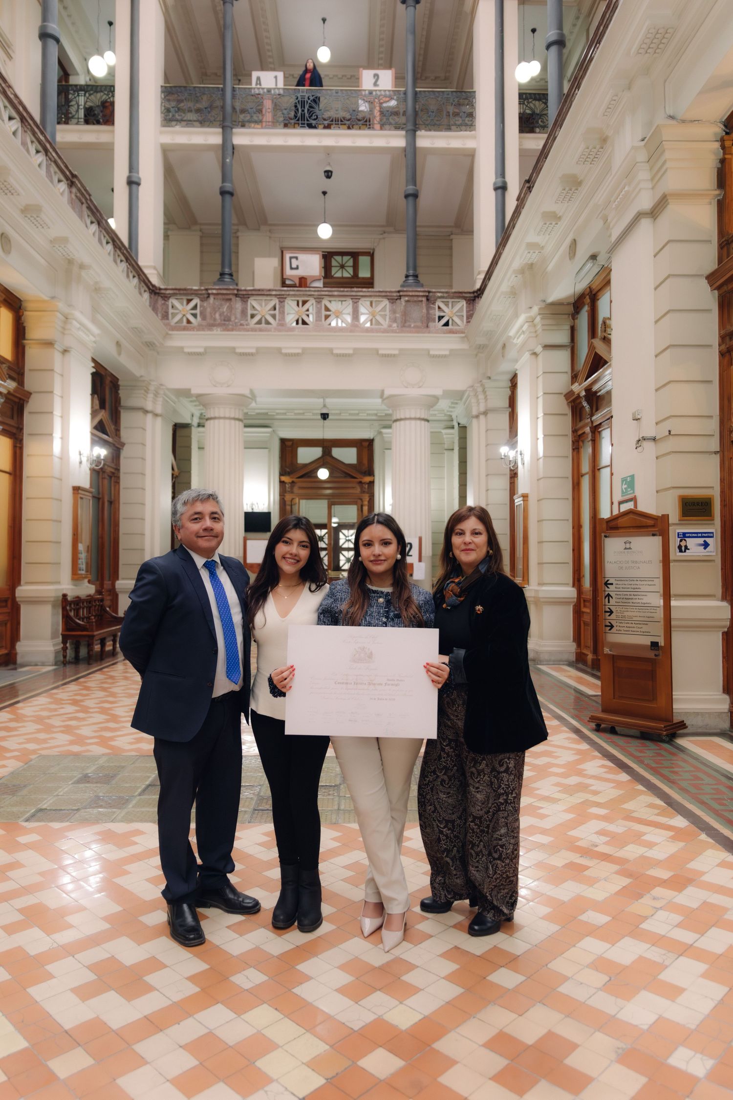 Four people pose with a certificate in a classical architectural hallway.