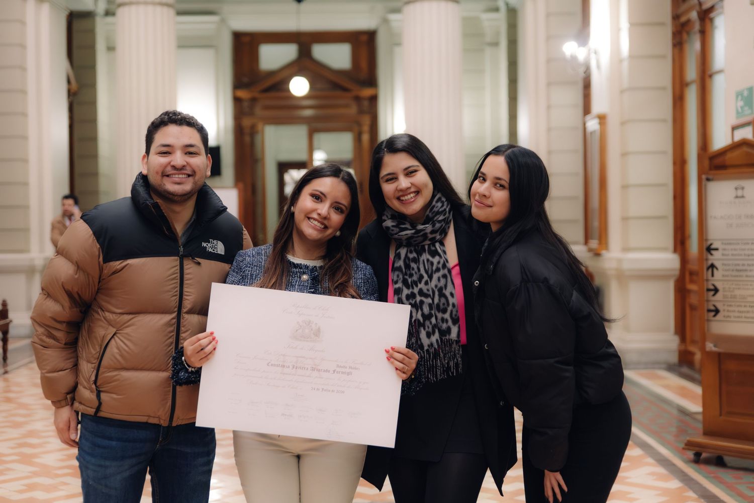 Four friends pose together with a formal certificate in a grand hall.