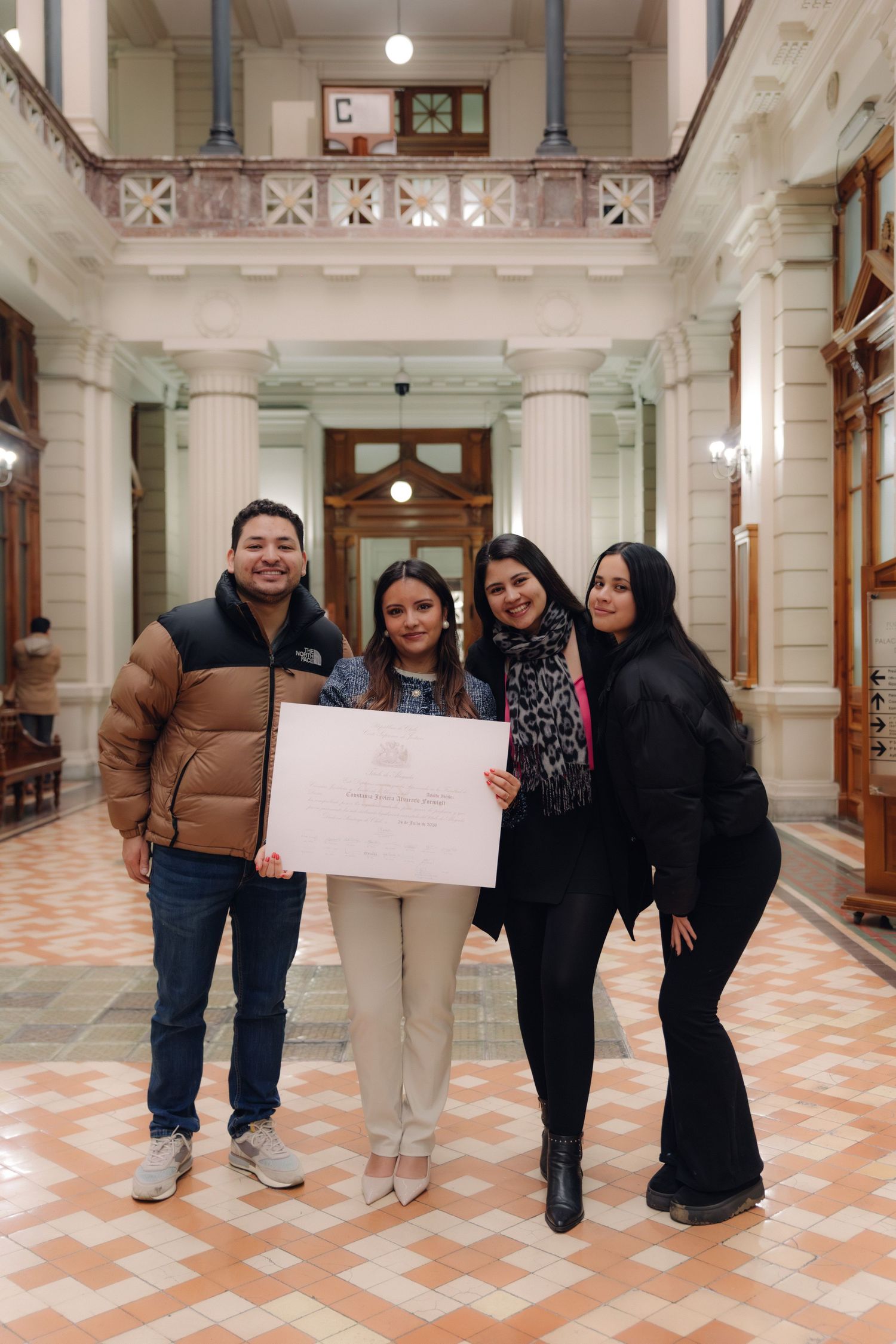 Four people proudly display a certificate in a classical columned hallway.