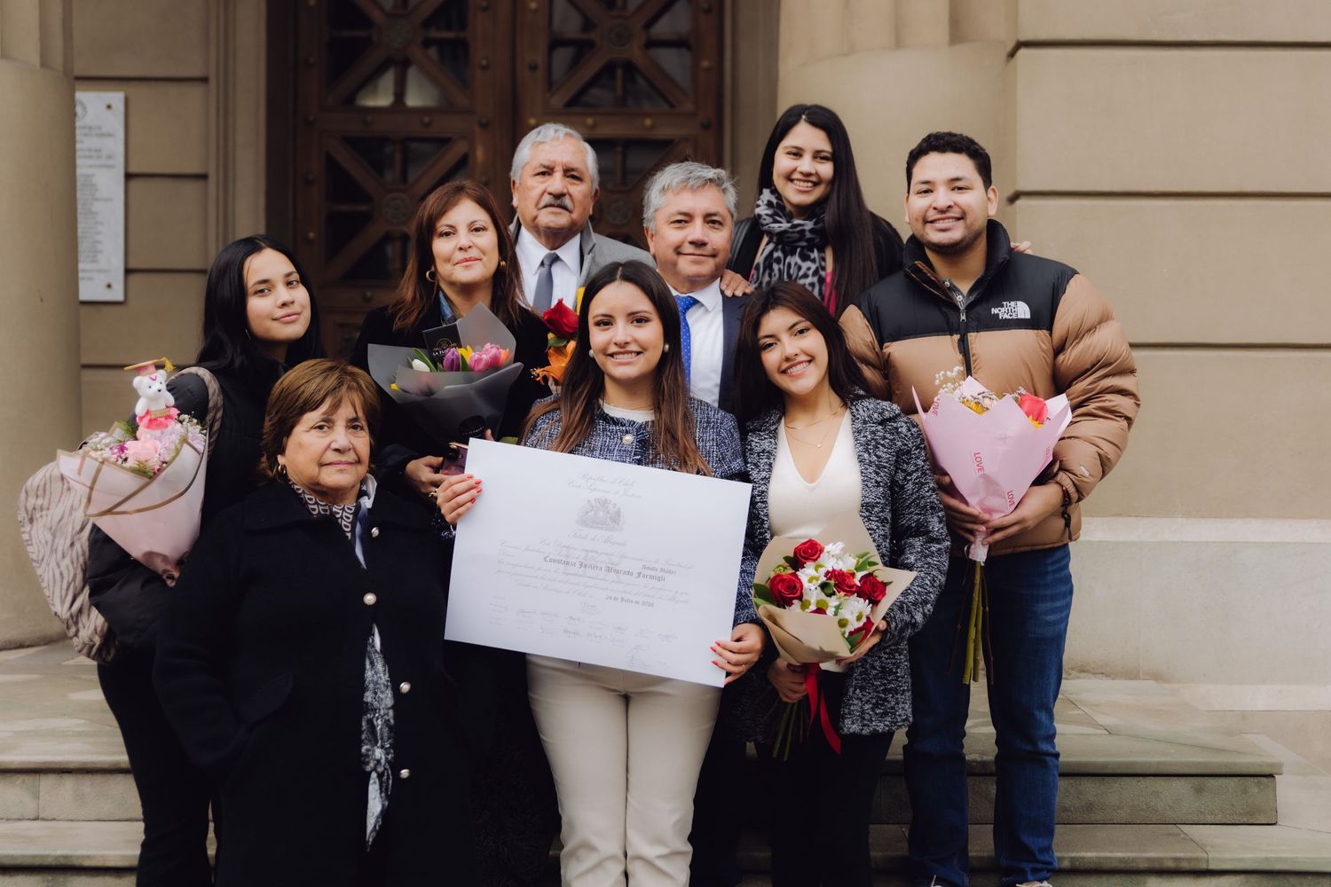 Happy family posing together on steps holding diploma and bouquets after graduation ceremony.