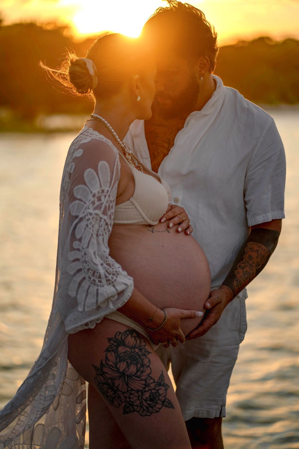 Un couple partage un tendre moment au coucher du soleil, dévoilant un ventre arrondi