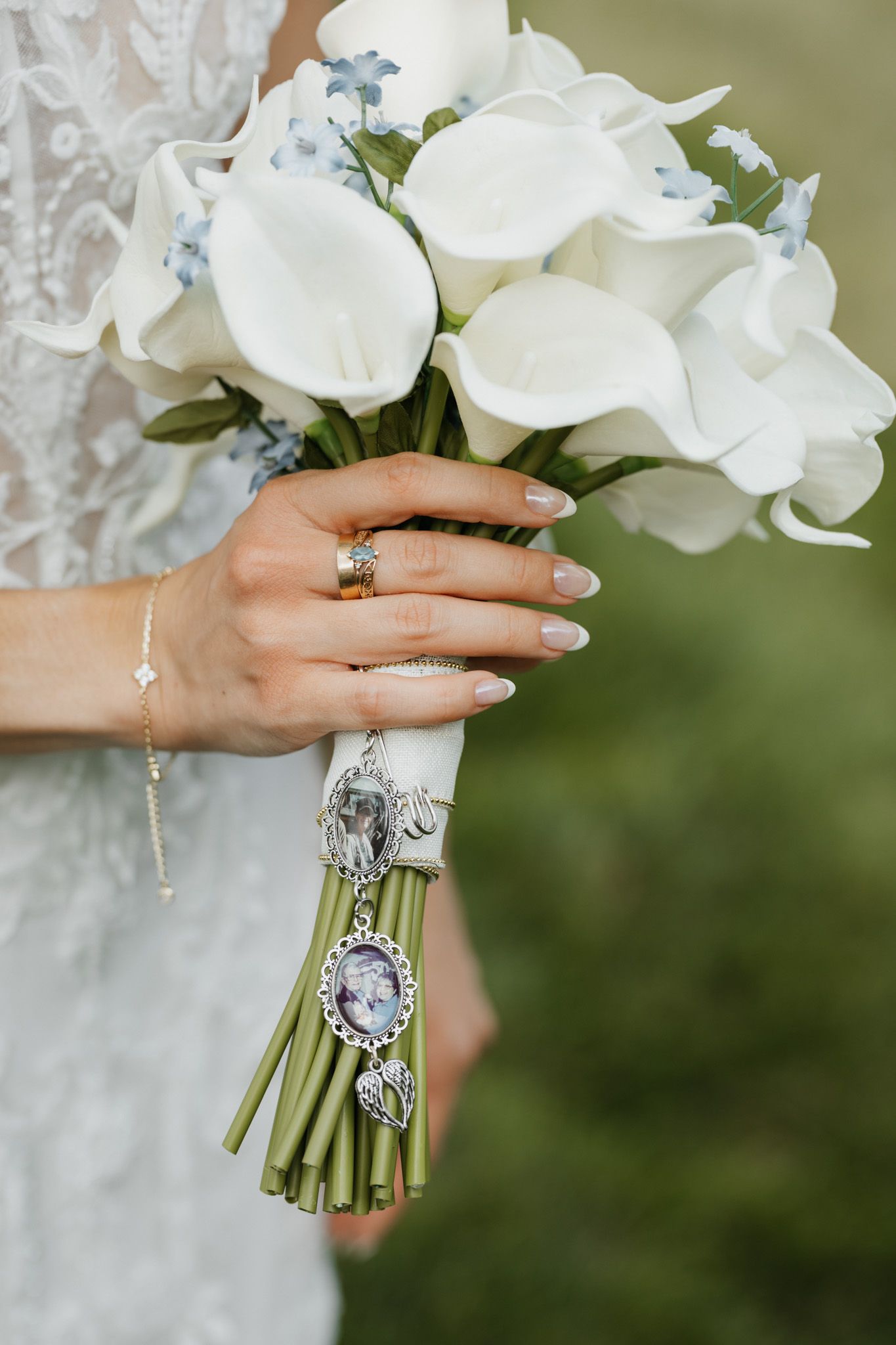 Bride holds white calla lily bouquet with silver memorial charm and wears gold ring and diamond bracelet.