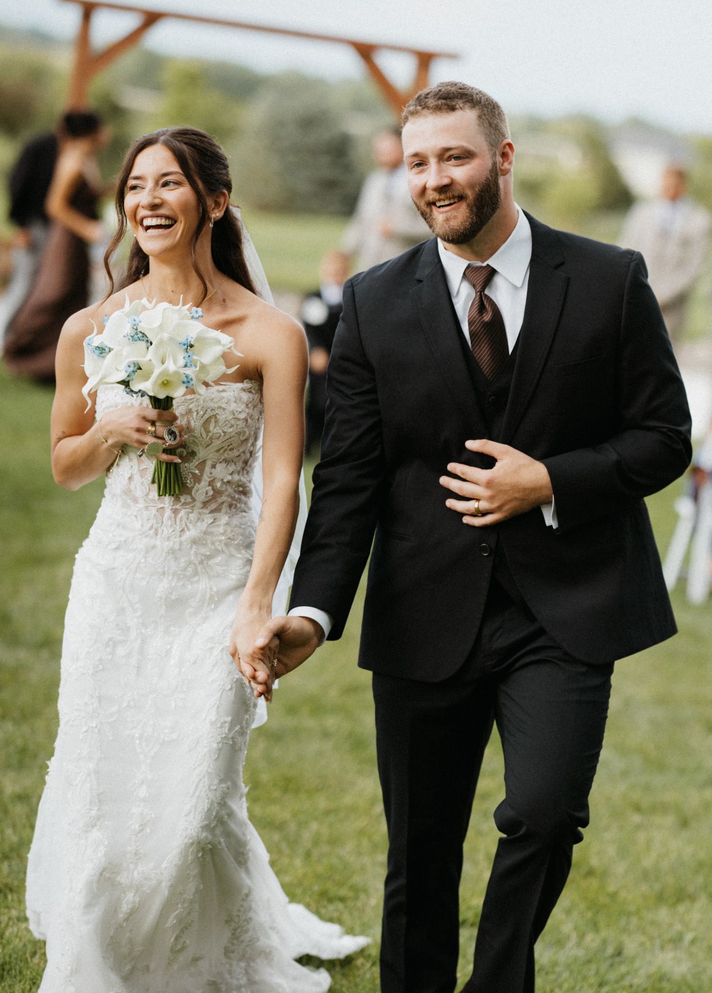 Joyful newlyweds walk hand in hand down the aisle after their outdoor wedding ceremony.