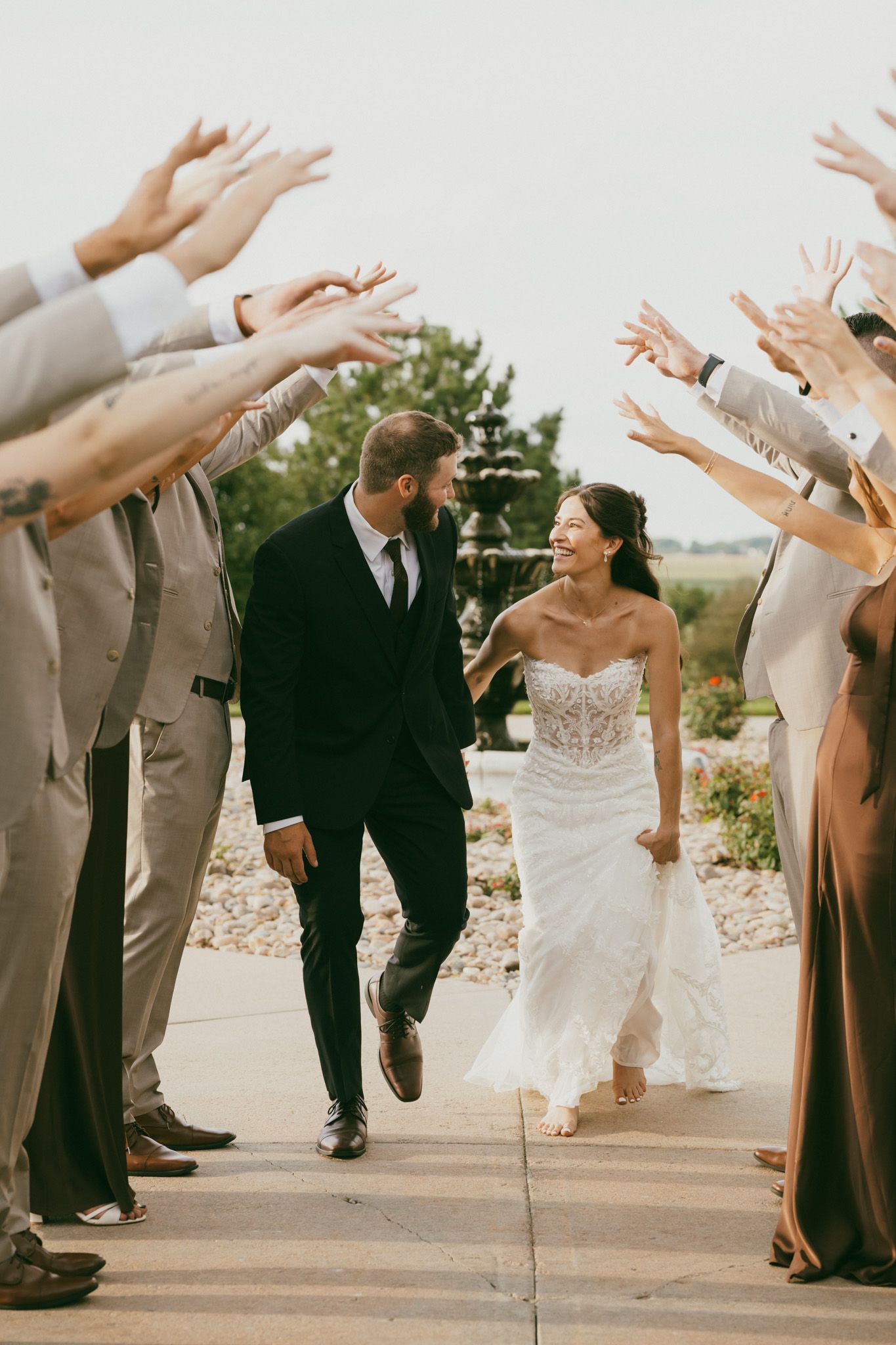 Newlyweds run through cheering wedding party tunnel in joyful outdoor ceremony exit celebration.