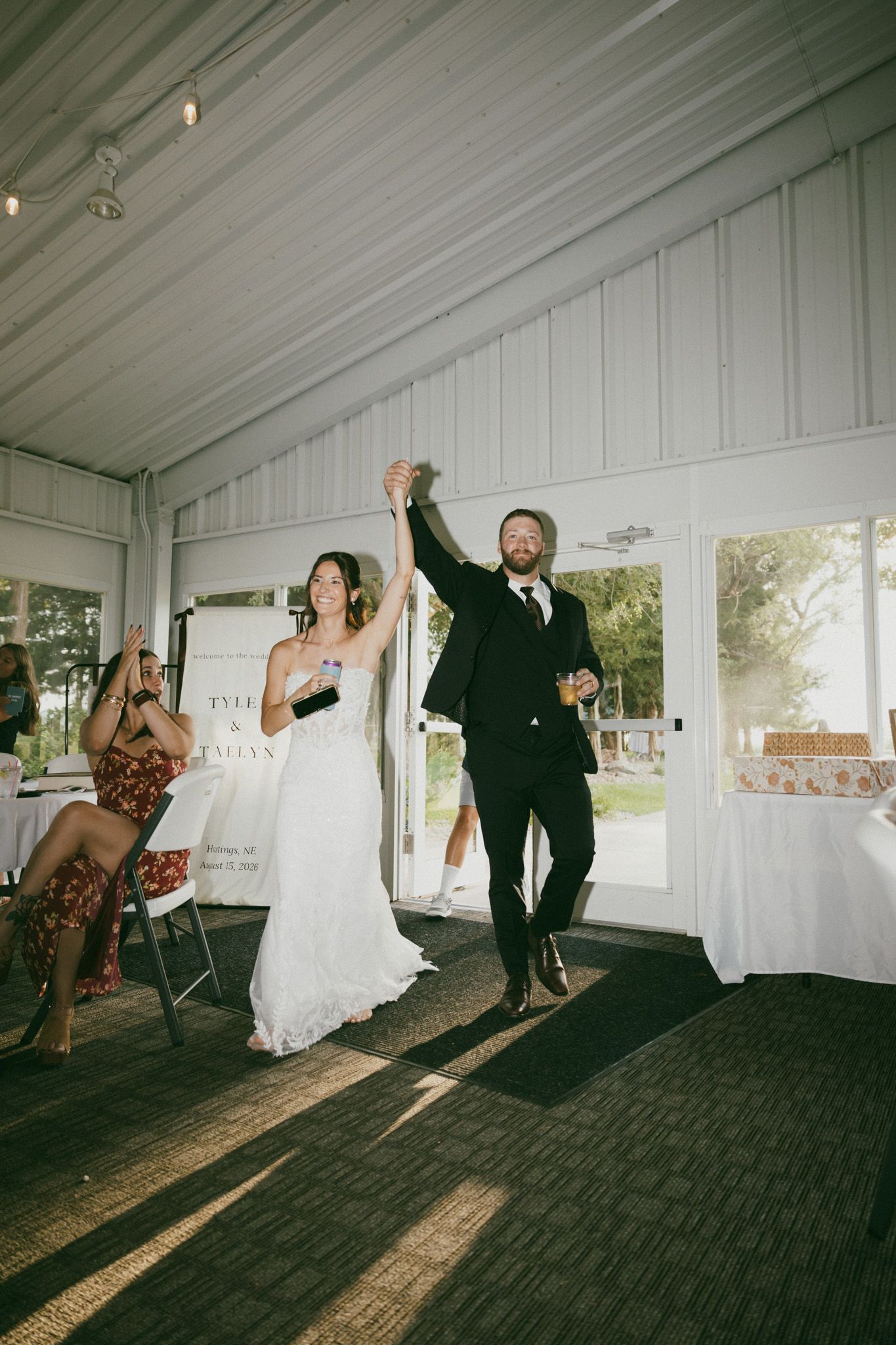 Bride and groom raising hands together at wedding reception in white tent venue.