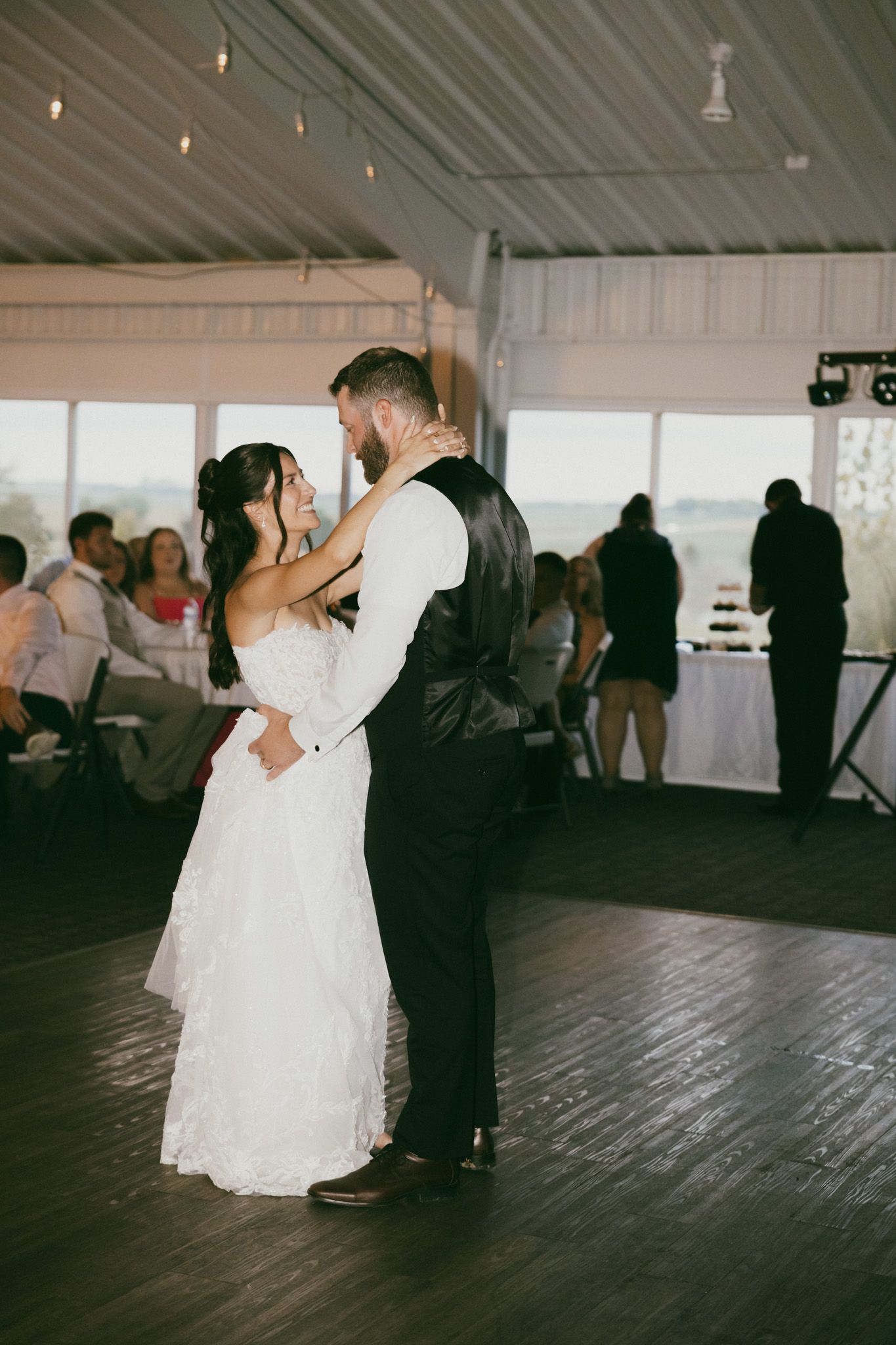 Bride and groom share their first dance at a wedding reception in a white tent venue with guests watching.