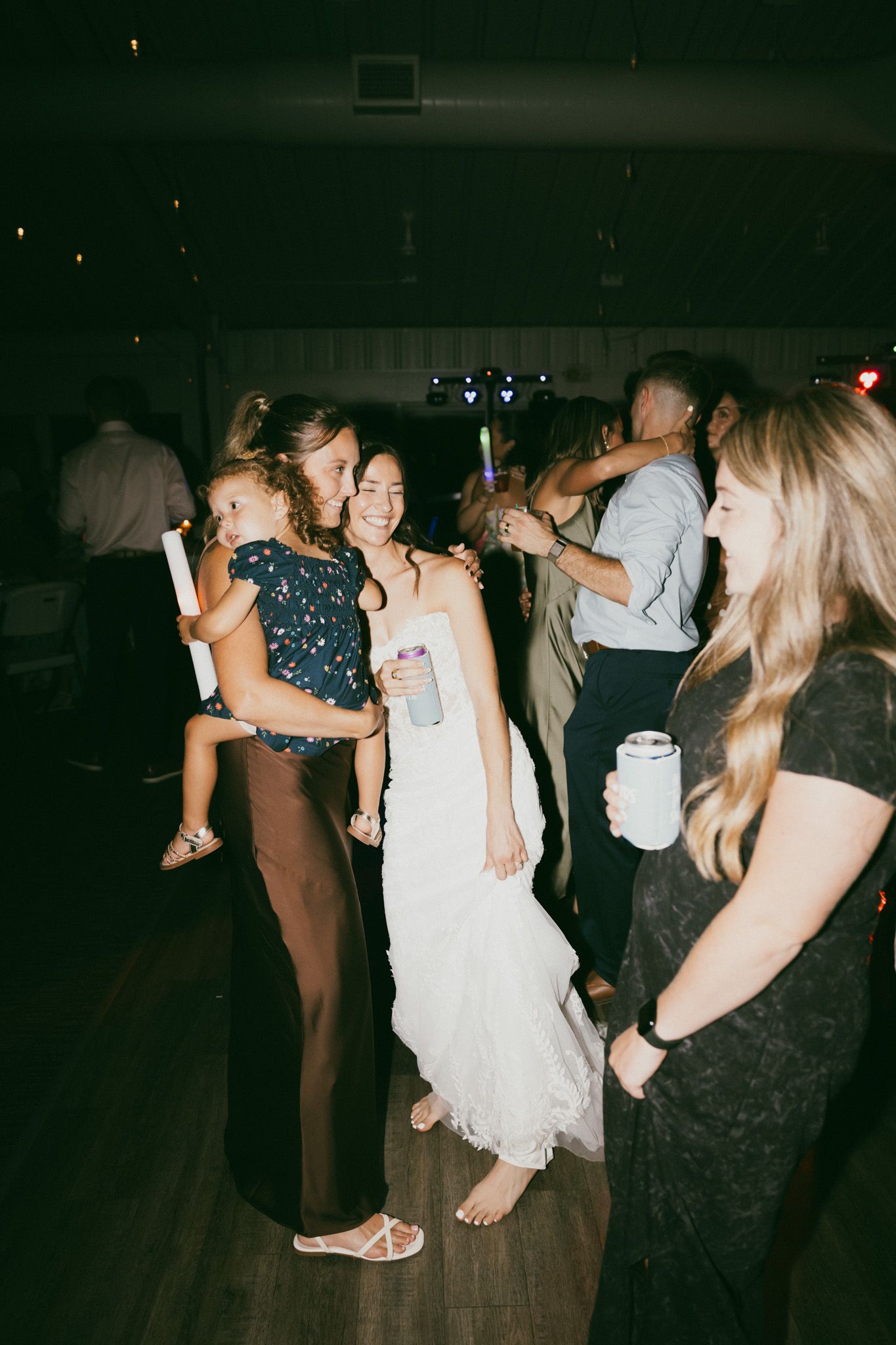 Bride in white lace gown dancing with guests at wedding reception on hardwood dance floor.