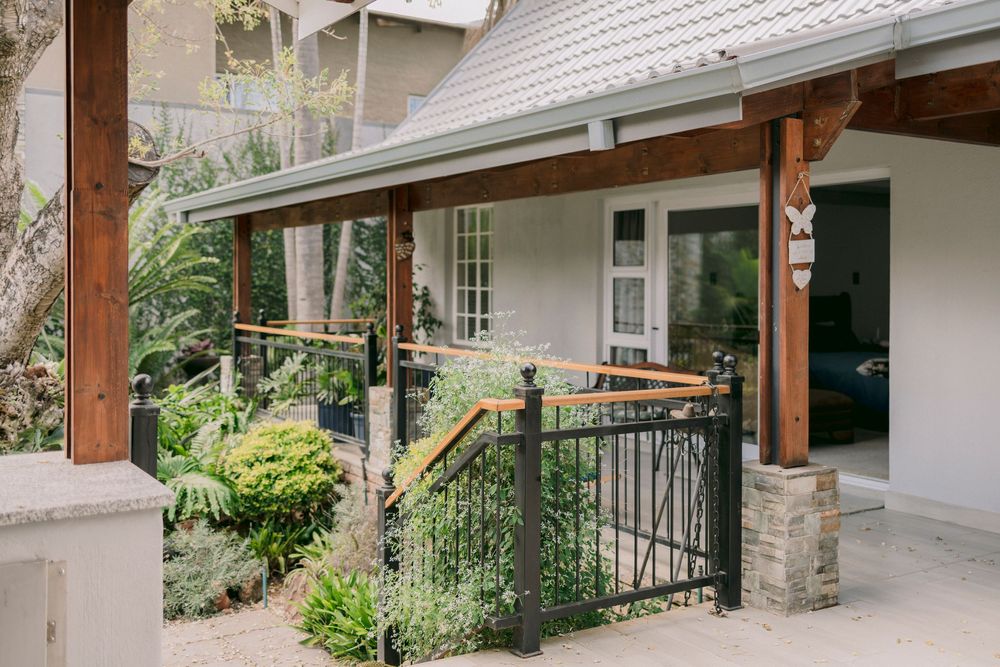 Charming cottage entrance with wooden pillars, black iron gate, and lush garden landscaping.