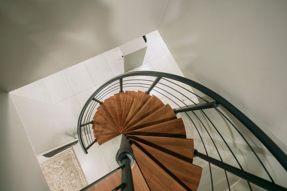 Aerial view of a modern spiral staircase with wooden steps and black metal railing in a white interior.