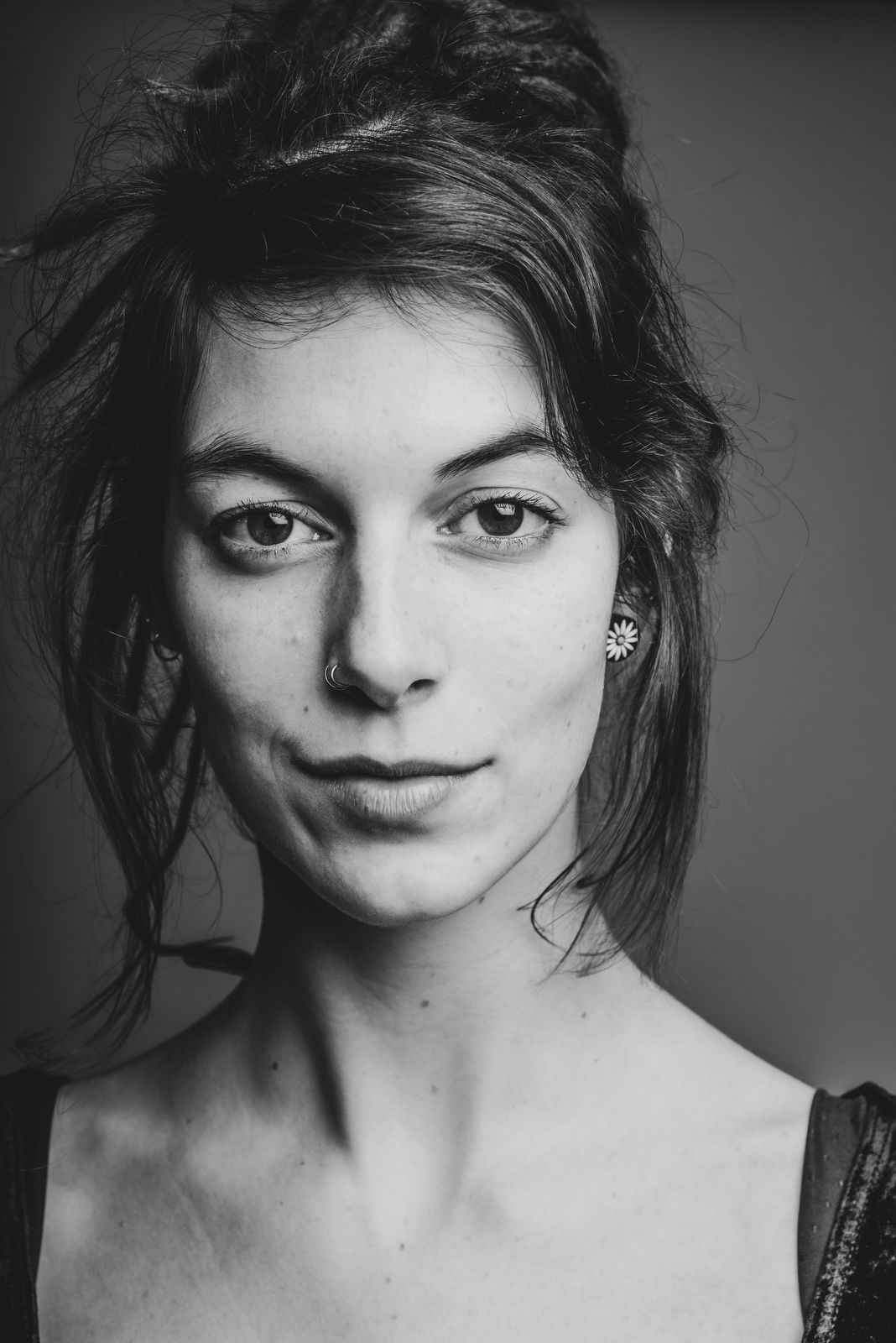 Frontaal zwart wit portret van een vrouw met dreadlocks en een neuspiercing, met een zachte glimlach in de studio van Bart Boodts
