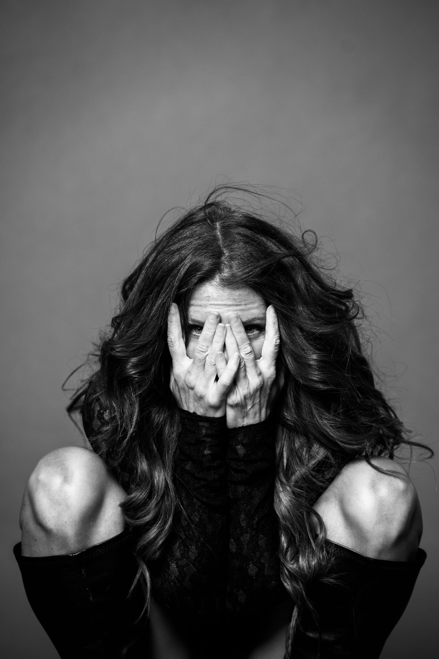 Black and white dramatic portrait of a woman covering her face with both hands, hair flowing.